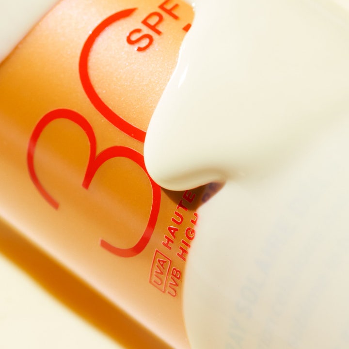 Nuxe Sun Spray SPF30 184 g aurinkovoidetta kasvoille kultaisessa pullossa veden väreilyn keskellä.