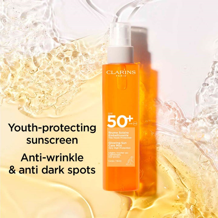 Clarins Glowing Sun Care Mist SPF50+ 150 ml aurinkosuoja oranssissa pullossa vesiroiskeiden keskellä.
