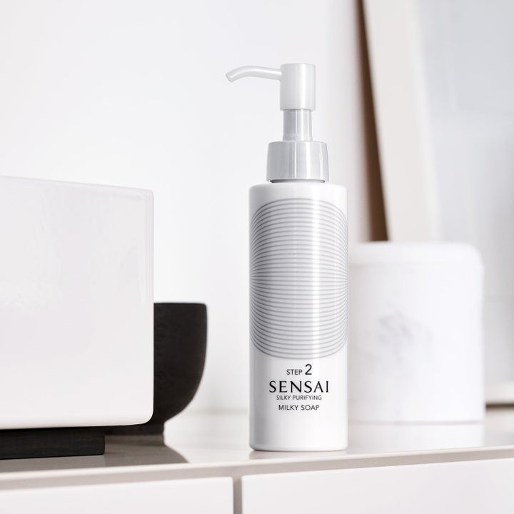 Sensai Silky Purifying Milky Soap puhdistustuote valkoinen pumppupullo harmaalla kuviolla vaaleassa tilassa.