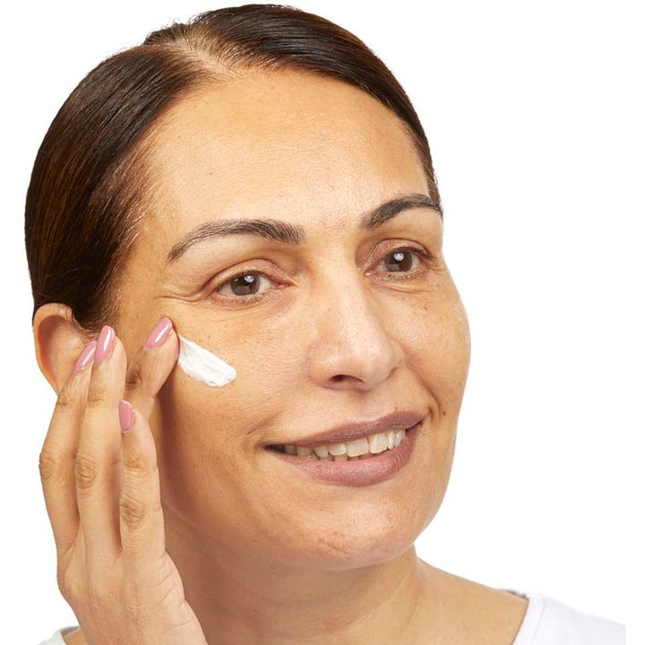 No7 Restore & Renew Multi Action Day Cream 50 ml kiinteyttävä päivävoide nainen levittämässä voidetta poskelle.