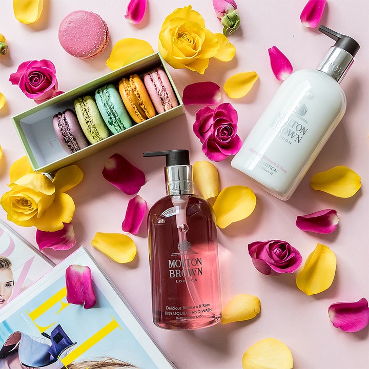 Molton Brown Delicious Rhubarb & Rose Hand Lotion 300 ml kosteuttaa keltaisten ja vaaleanpunaisten ruusujen keskellä.