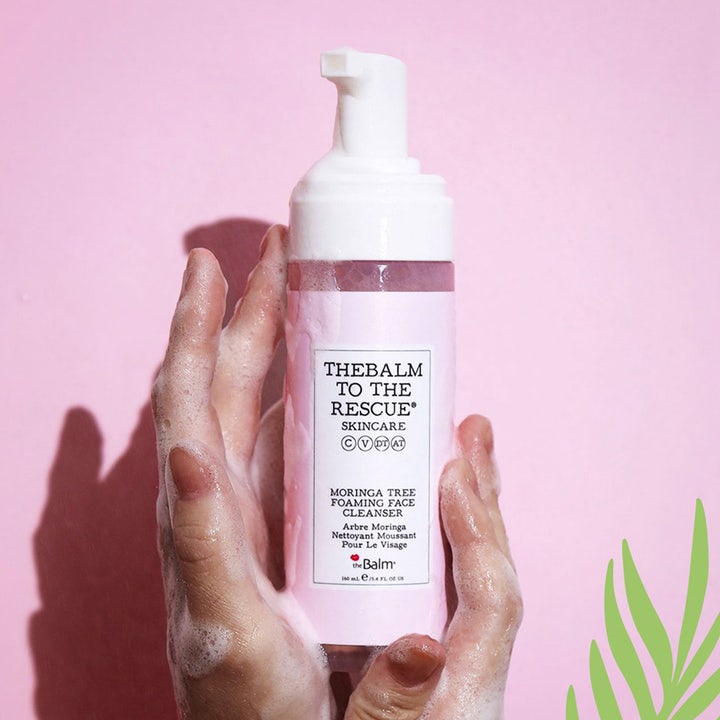 theBalm to the Rescue Moringa Tree 150 ml puhdistusvaahto puhdistaa ihon vaaleanpunaisessa pullossa vaahtoisissa käsissä