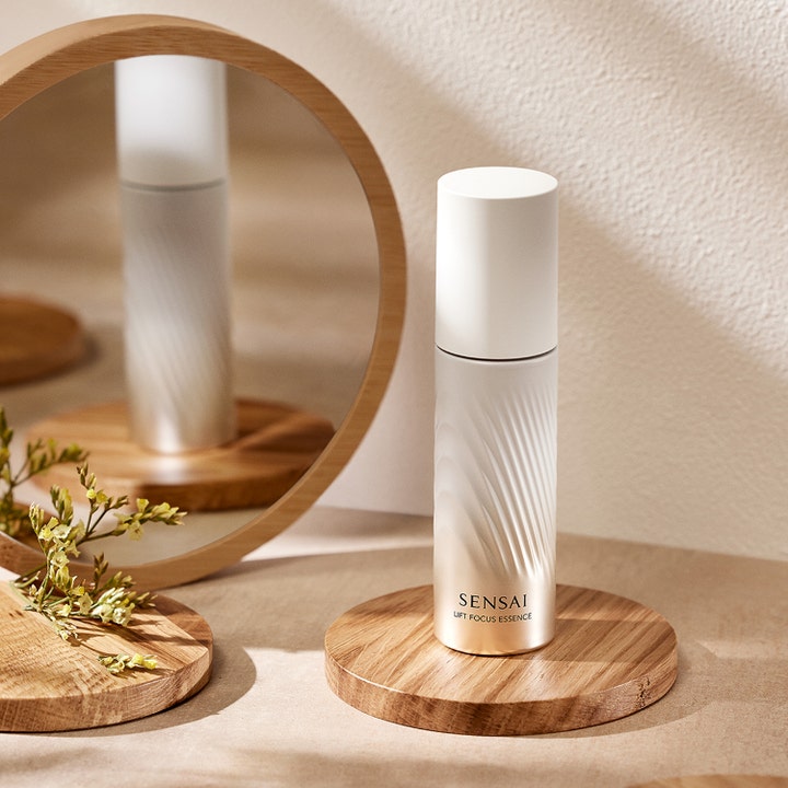 Sensai Lift Focus Essence 40 ml kiinteyttävä seerumi helmiäisvalkoisessa pullossa puualustalla peilin edessä.