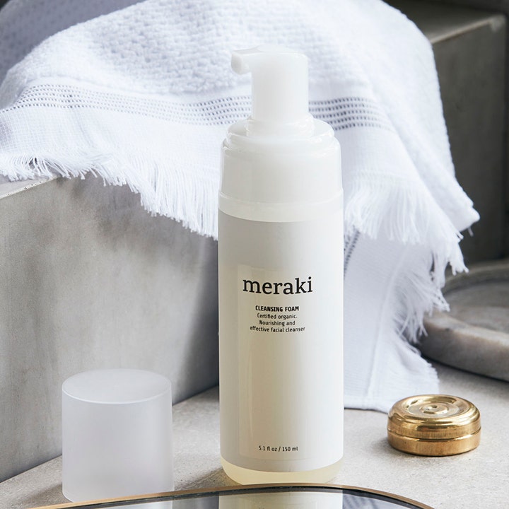 Meraki Cleansing Foam 150 ml ravitseva puhdistusvaahto valkoisessa pumppupullossa valkoisen pyyhkeen edessä