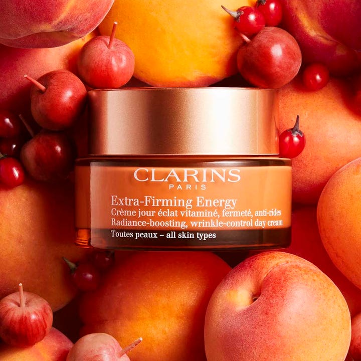 Clarins Extra-Firming Energy 50 ml heleyttävä päivävoide oranssissa purkissa persikoiden ja marjojen ympäröimänä.
