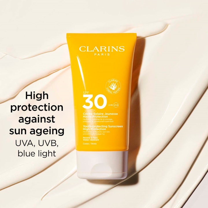 Clarins Youth-protecting Sunscreen 150 ml SPF30 aurinkovoide keltaisessa tuubissa vaalean voiteen päällä.