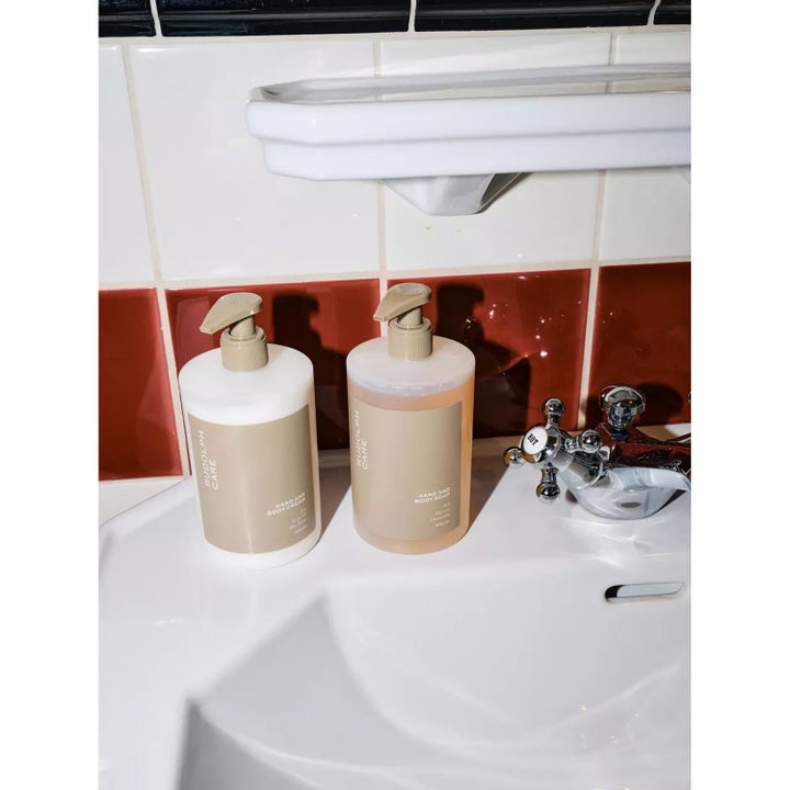 Rudolph Care Hand And Body Soap 500 ml puhdistava suihkusaippua beigellä etiketillä pesualtaan reunalla.