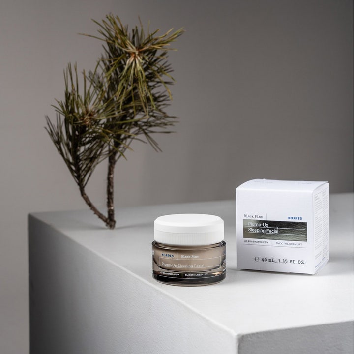 KORRES Black Pine Plump-Up Sleeping Facial 40 ml yövoide ruskeassa lasipurkissa ja valkoinen pakkaus männynoksan vieressä.