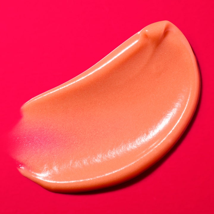 Nuxe Merveillance Lift Glow 50 ml kiinteyttävä päivävoide ja sen heleyttävä persikkainen koostumus pinkillä taustalla.