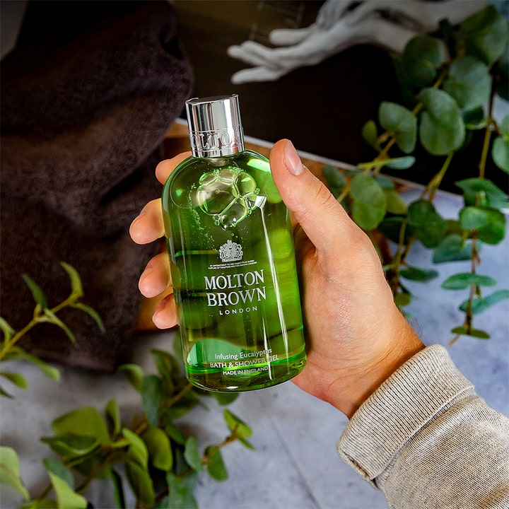 Molton Brown Infusing Eucalyptus Bath & Shower Gel 300 ml virkistävä suihkugeeli kädessä eukalyptuksen lehtien ympäröimänä