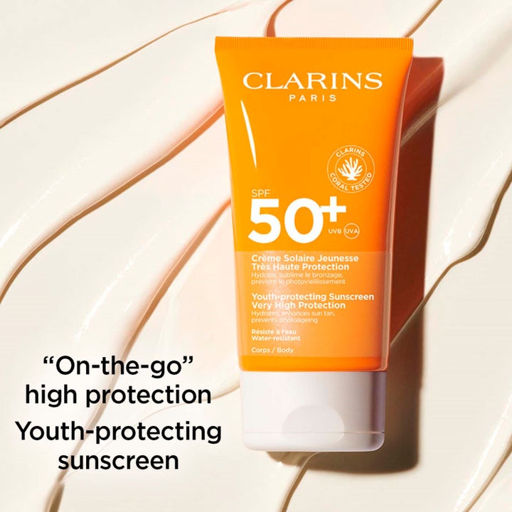Clarins Youth-protecting Sunscreen 150 ml korkea suoja SPF50+ oranssi tuubi suojaa ihoa voidemaisella taustalla
