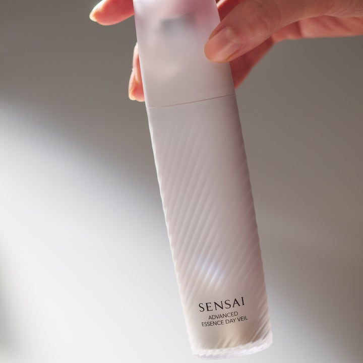 Sensai Advanced Essence Day Veil 40 ml suojaseerumi kädessä vaaleassa uurretussa hylsyssä.