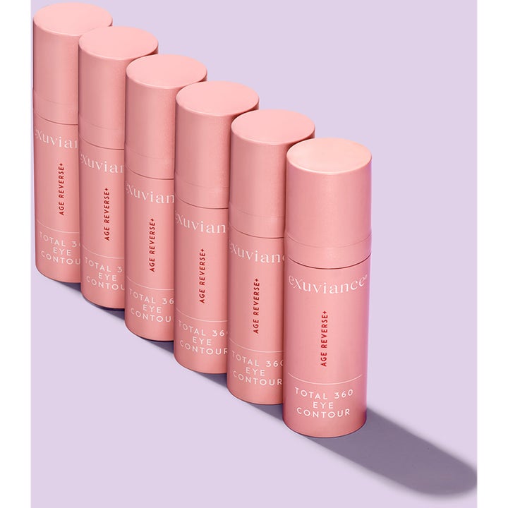 Exuviance Age Reverse Eye Contour 15 g silmänympärysvoide kuusi vaaleanpunaista pumppupulloa rivissä liilalla taustalla
