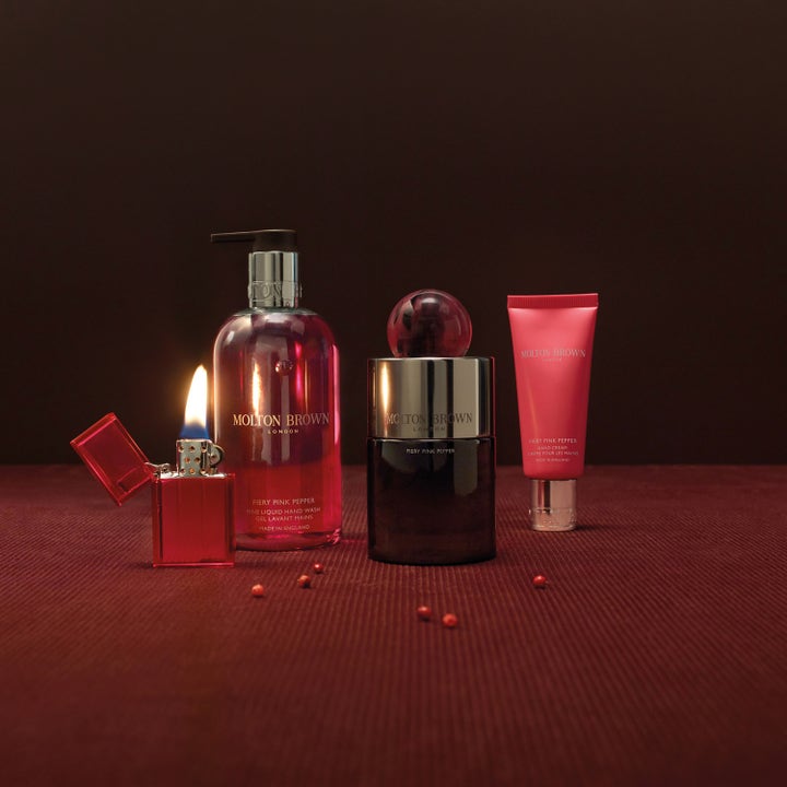 Molton Brown Fiery Pink Pepper 300 ml käsisaippua pumppupullossa muiden sarjan tuotteiden ja liekin rinnalla.