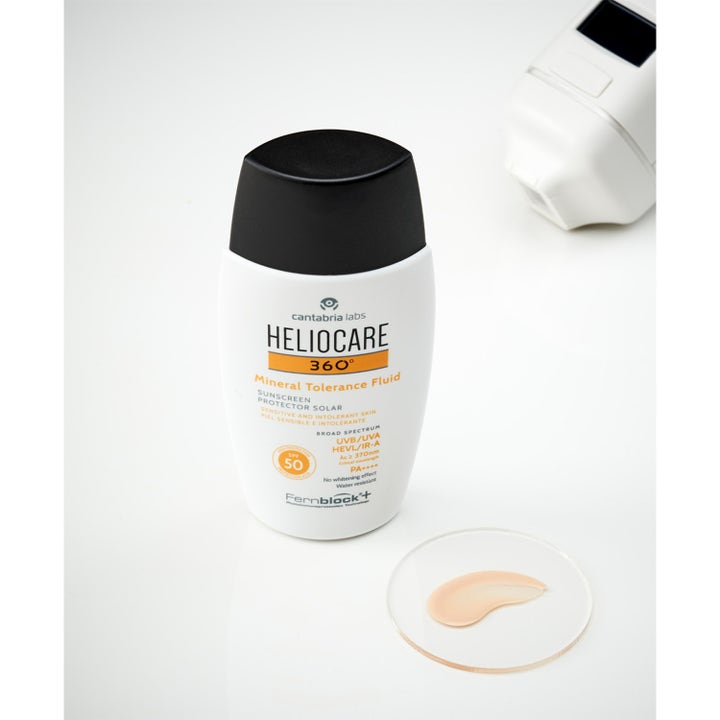 Heliocare Mineral Tolerance Fluid SPF 50 50 ml suojaava aurinkovoide ja beige voidekoostumus lasilevyllä.