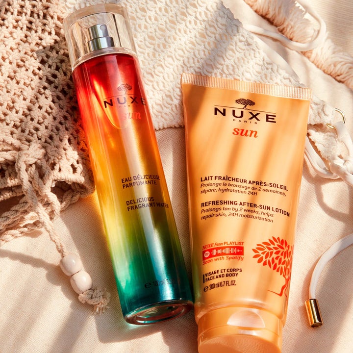 Nuxe Sun Kit After Sun 200 ml kosteuttava voide ja värikäs tuoksuvesi 100 ml aseteltuna vaalealle neulekassille.