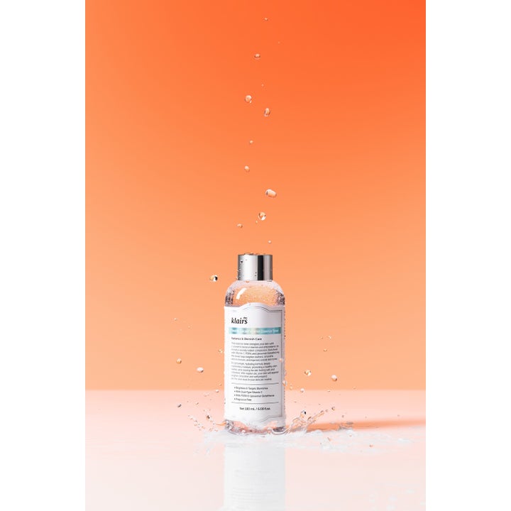 Klairs Freshly Juiced Vitamin Essence Toner 180 ml kirkastava kasvovesi hopeisella korkilla vesiroiskeiden keskellä.