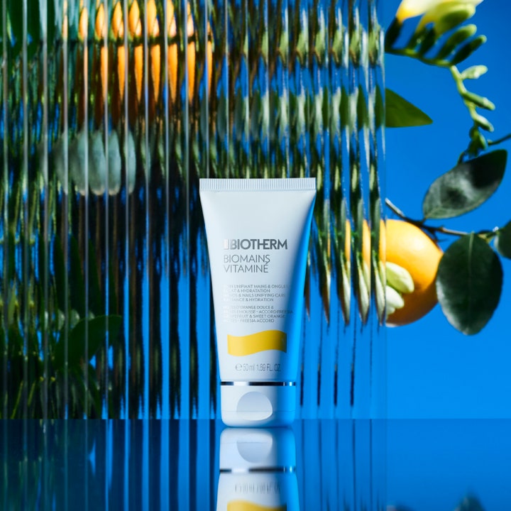 Biotherm Biomains Vitaminé 50 ml kosteuttava käsivoide tuubissa appelsiinin ja vihreiden lehtien ympäröimänä.