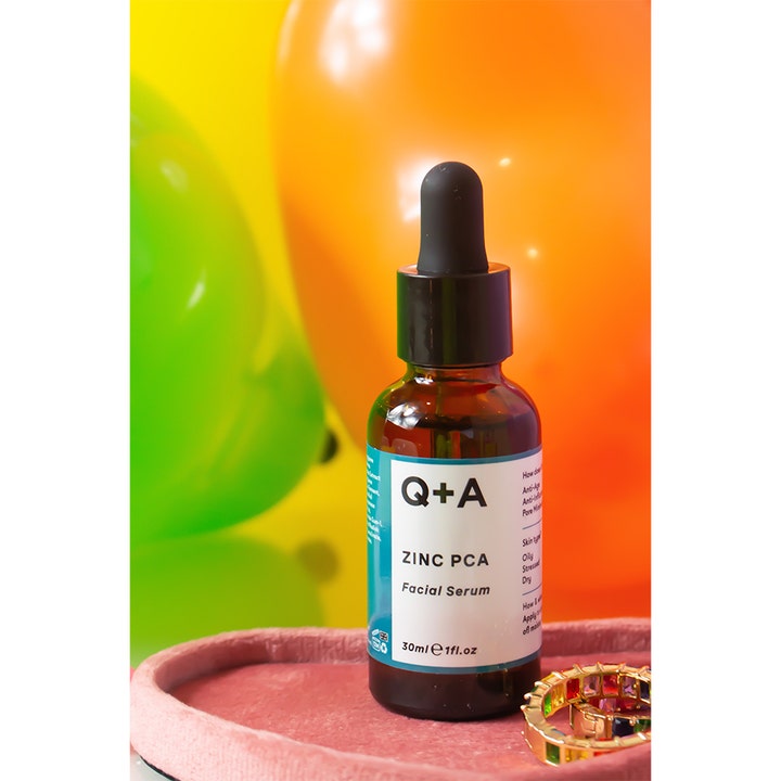 Q+A Zinc PCA Facial Serum 30 ml epäpuhtauksia ehkäisevä kasvoseerumi ruskeassa lasipullossa värikkäiden ilmapallojen edessä.