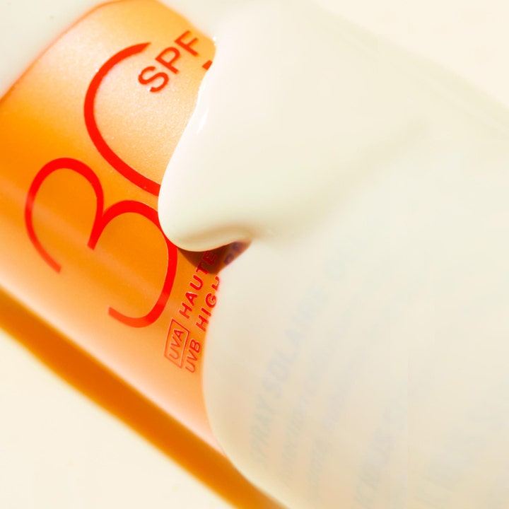 Nuxe Sun Spray SPF30 184 g aurinkosuoja, jonka täyteläinen valkoinen voidekoostumus valuu oranssin pullon päällä.