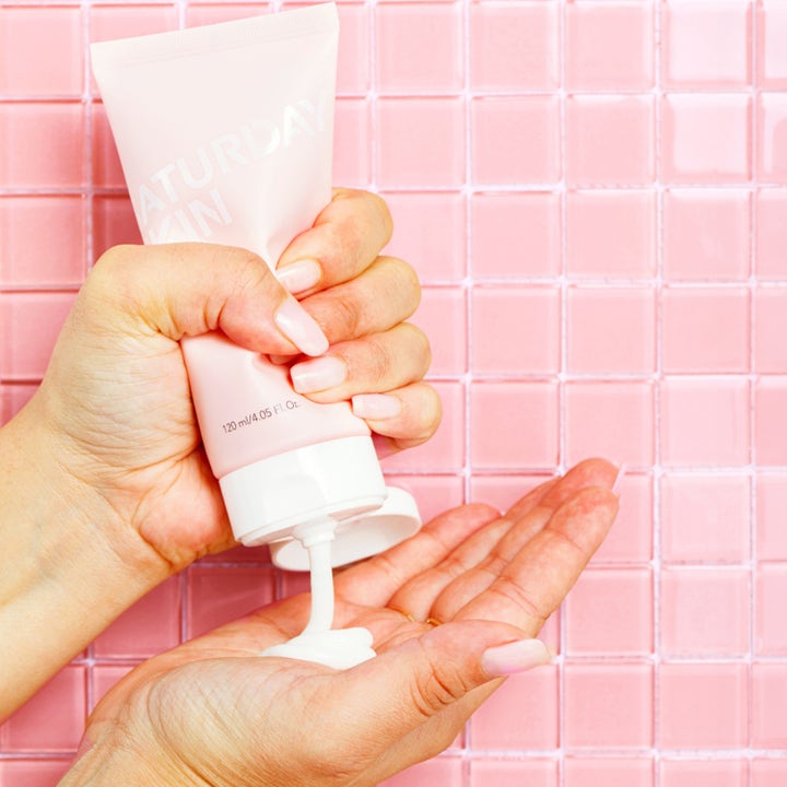 Saturday Skin Rise + Shine Gentle Cleanser 120 ml puhdistusvoide puristetaan kämmenelle vaaleanpunaisella laatalla.