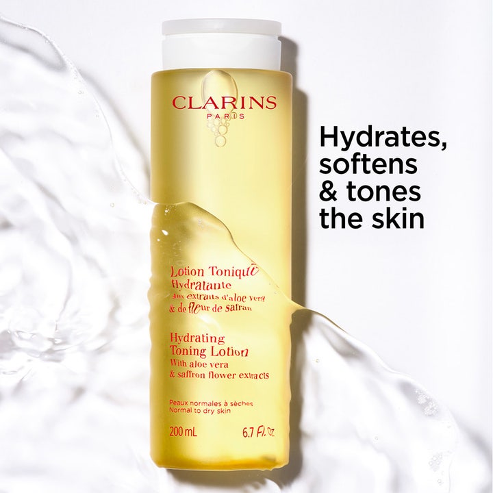 Clarins Hydrating Toning Lotion 400 ml kosteuttava kasvovesi keltaisessa pullossa vesiroiskeiden keskellä.