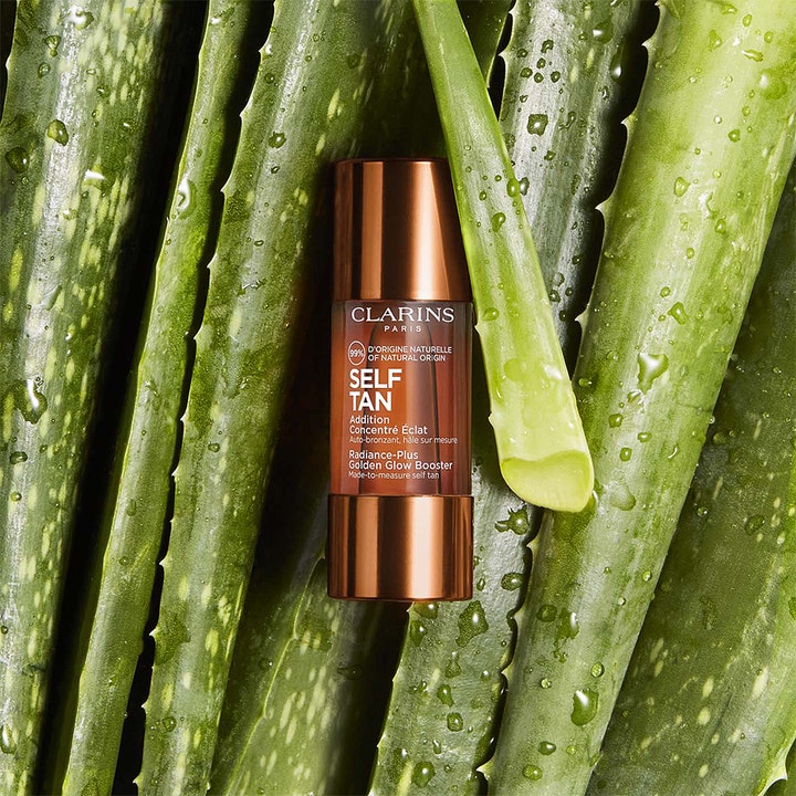 Clarins Radiance-Plus Golden Glow Booster Face 15 ml itseruskettavat tipat ruskeassa pullossa aloe vera -lehtien päällä.