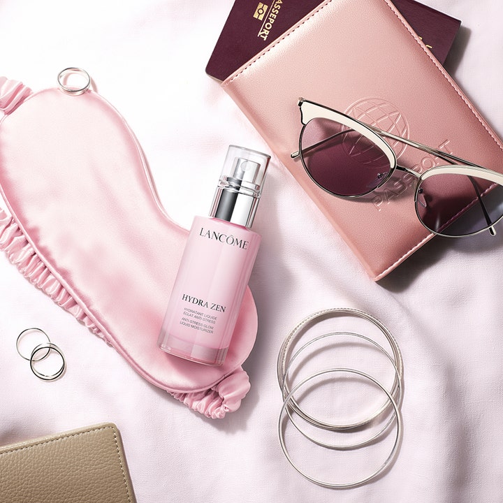 Lancôme Hydra Zen Liquid Moisturizer 50 ml kosteuttava päivävoide vaaleanpunaisessa pullossa unimaskin ja asusteiden kera.
