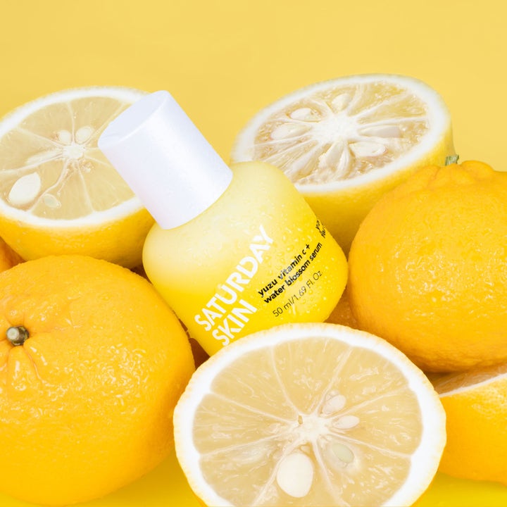 Saturday Skin Yuzu Vitamin C + Water Blossom Serum 50 ml heleyttävä seerumi keltaisessa pullossa yuzu-hedelmien keskellä.
