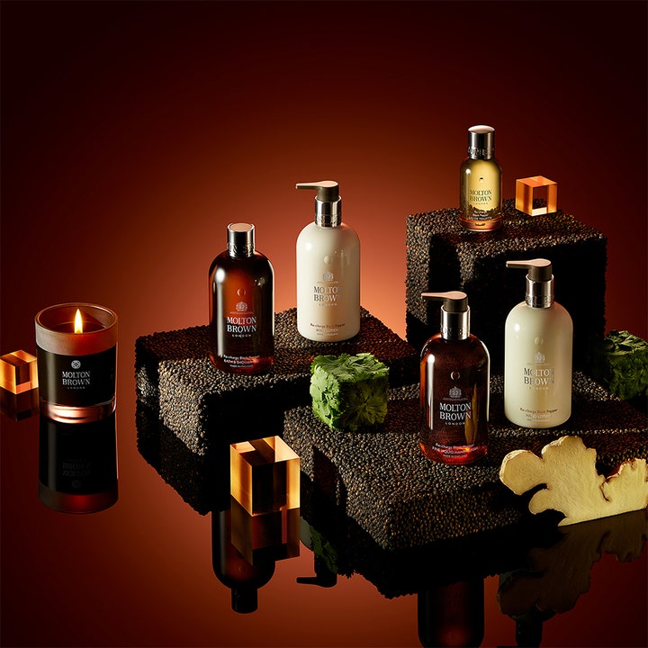 Molton Brown Black Peppercorn Body Lotion 300 ml kosteuttava vartalovoide mausteisessa asetelmassa kynttilän kera.
