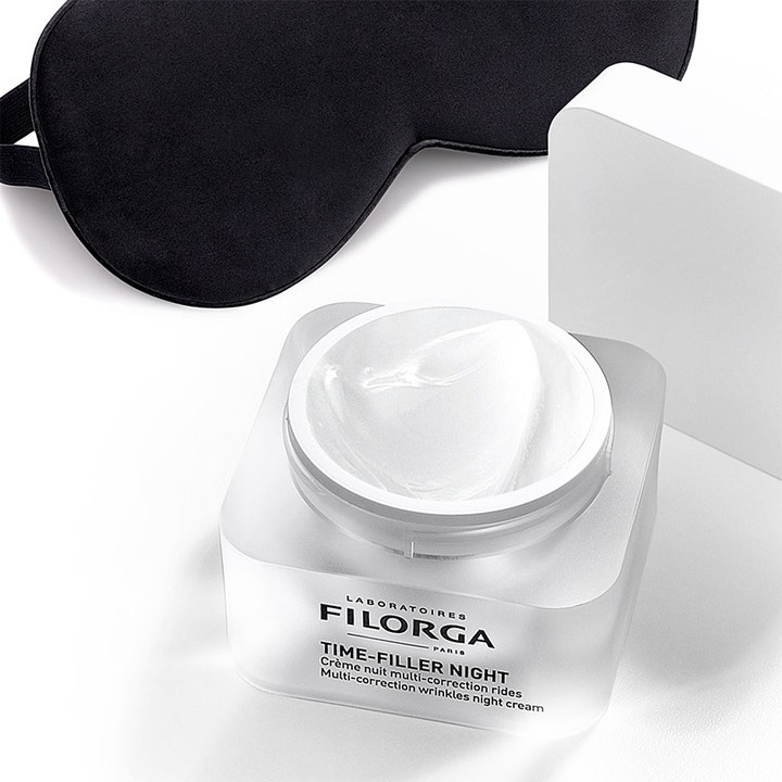 Filorga Time-Filler Night 5 XP 50 ml silottava yövoide avatussa lasipurkissa mustan unimaskin rinnalla.