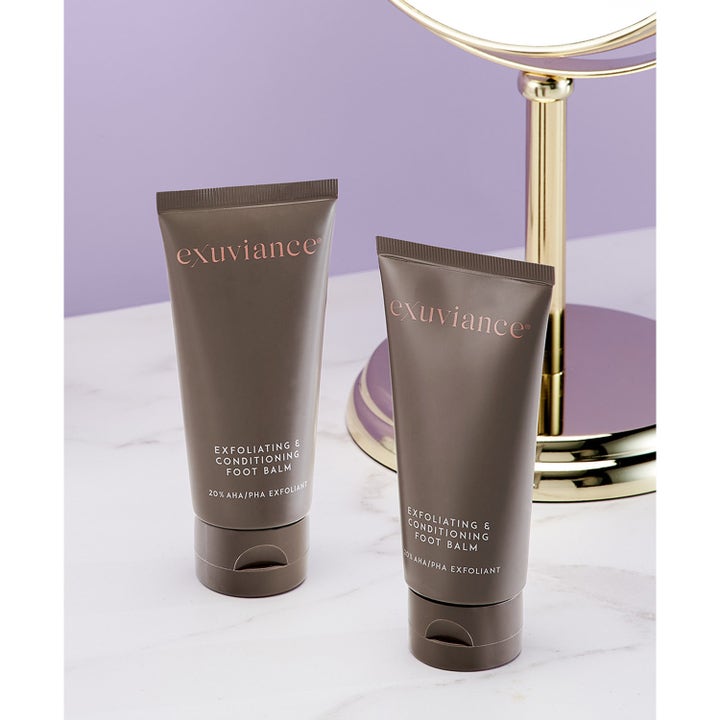 Exuviance Exfoliating & Conditioning Foot Balm 50 g kuoriva jalkavoide ruskeissa tuubeissa marmorilla peilin edessä.