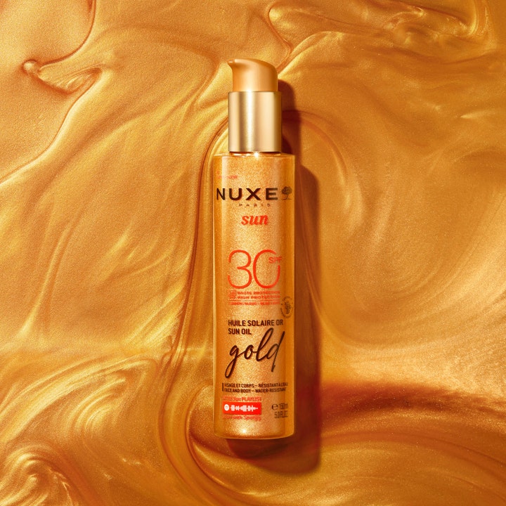 Nuxe Sun Tanning Oil Gold SPF30 150 ml suojaava aurinkoöljy kultaisessa pumppupullossa kimaltavalla taustalla