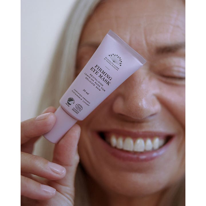 Rudolph Care Firming Eye Mask Leave On 20 ml kiinteyttävä silmänympärysnaamio vaaleanpunaisessa tuubissa naisen pitelemänä.