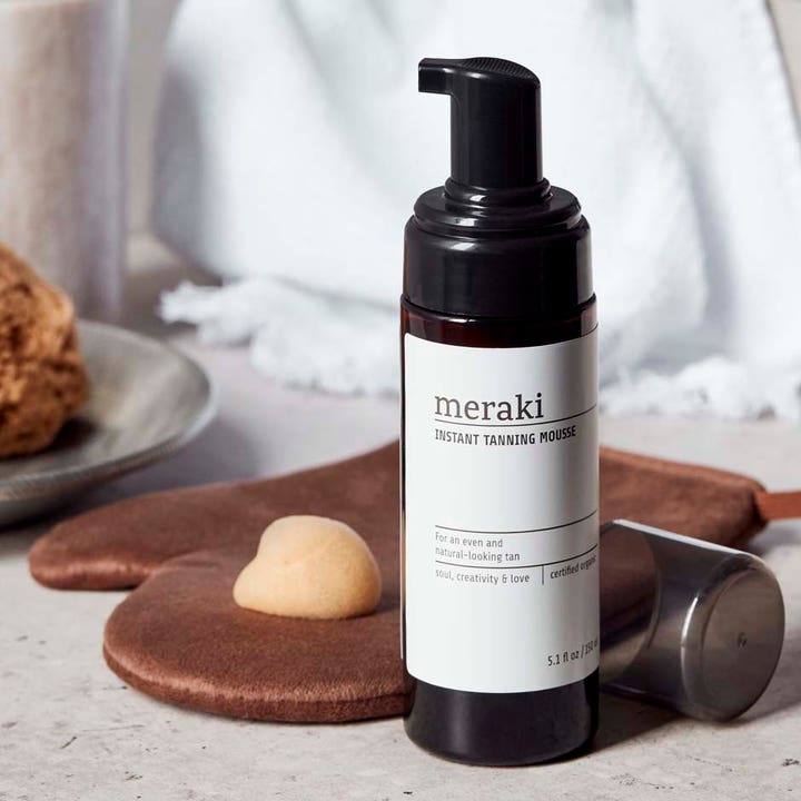 Meraki Instant Tanning Mousse 150 ml itseruskettava vaahto tummassa pullossa levityskäsineen päällä.