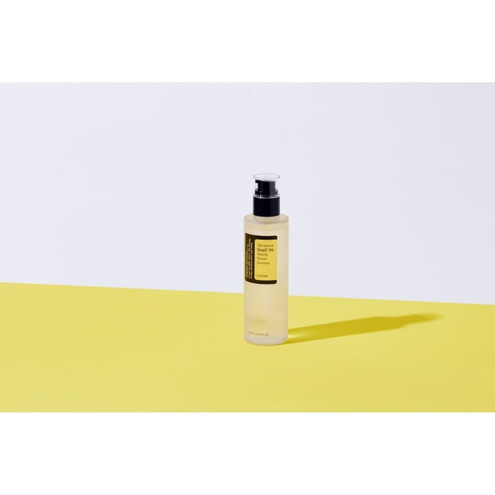 COSRX Advanced Snail 96 Essence 100 ml etanalimaa sisältävä hoitoneste kirkkaassa pullossa keltaisella taustalla.