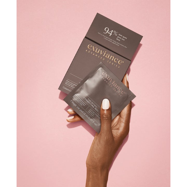 Exuviance Pure Retinol Correcting Peel 6 kpl uudistava kuorinta kädessä vaaleanpunaista taustaa vasten