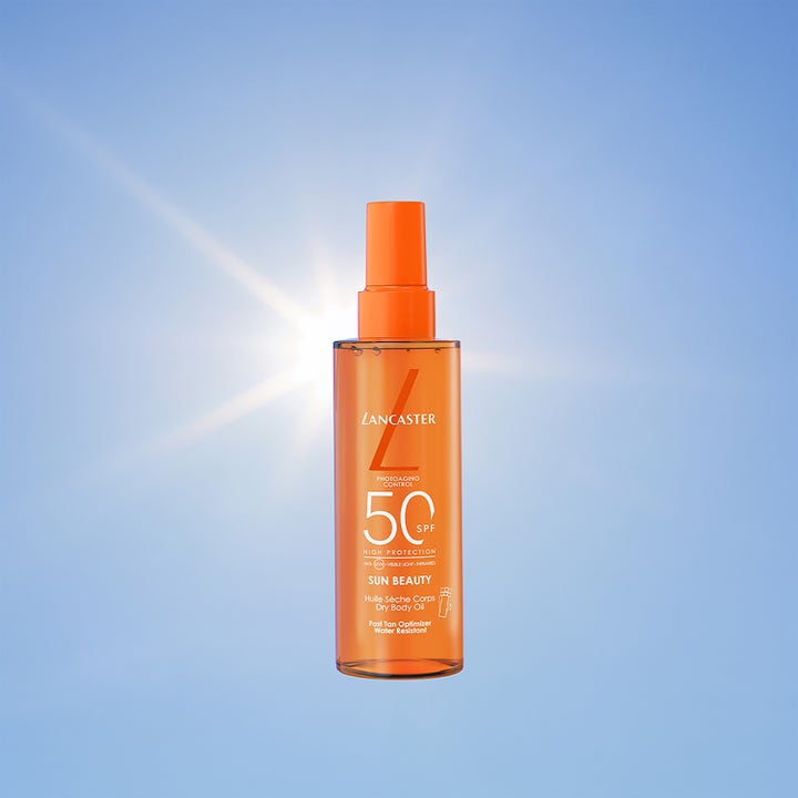 Lancaster Sun Beauty Dry Body Oil 150 ml SPF50 aurinkosuojaöljy oranssissa suihkepullossa aurinkoa ja taivasta vasten.