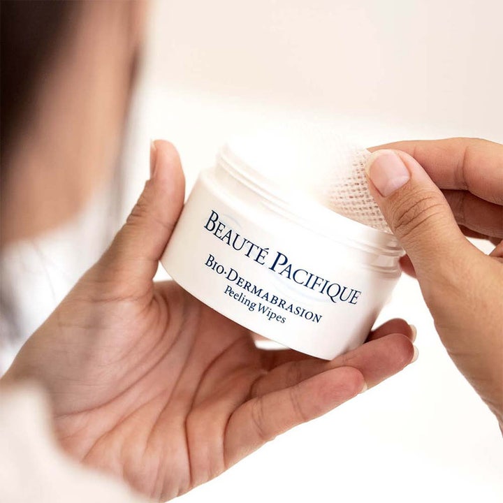 Beauté Pacifique Bio-Dermabrasion Peeling Wipes heleyttävät kuorintalaput valkoisessa purkissa, josta käsi nostaa yhden lapun.