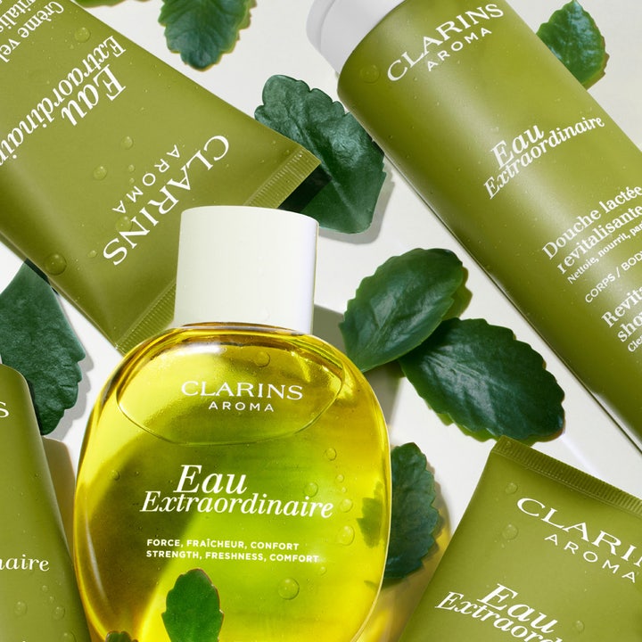 Clarins Eau Extraordinaire 200 ml virkistävä suihkuvoide vihreiden tuubien ja lehtien ympäröimänä vesipisaroilla.