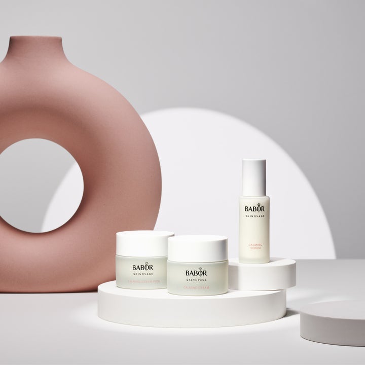 Babor Calming Serum 30 ml rauhoittava seerumi lasipullossa valkoisella alustalla vaaleanpunaisen maljakon vieressä.