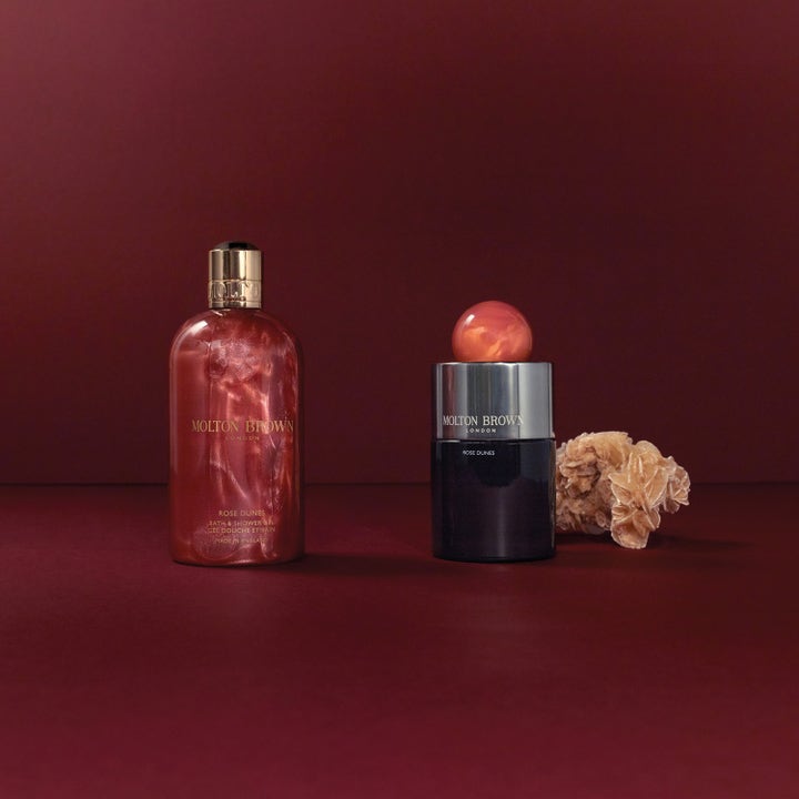 Molton Brown Rose Dunes Bath & Shower Gel 300 ml ylellinen suihkugeeli hohtavassa pullossa aavikkoruusun rinnalla.