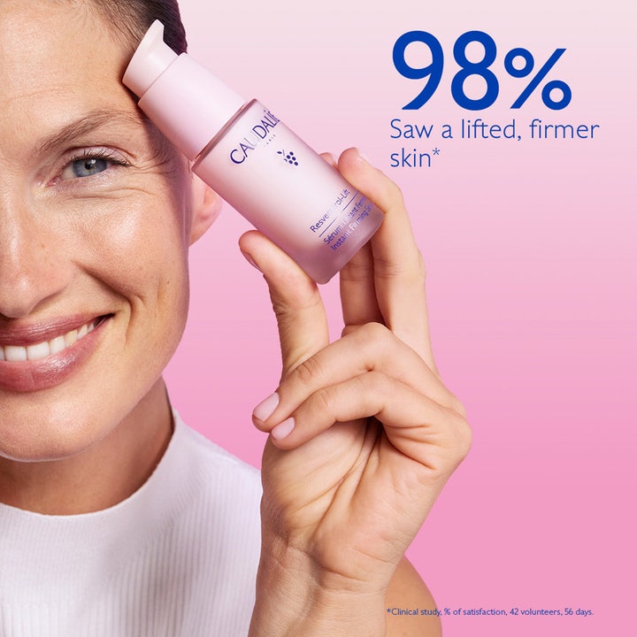 Caudalie Resveratrol-Lift Instant Firming Serum 30 ml kiinteyttävä seerumi vaaleanpunaisessa pullossa hymyilevän naisen kädessä.