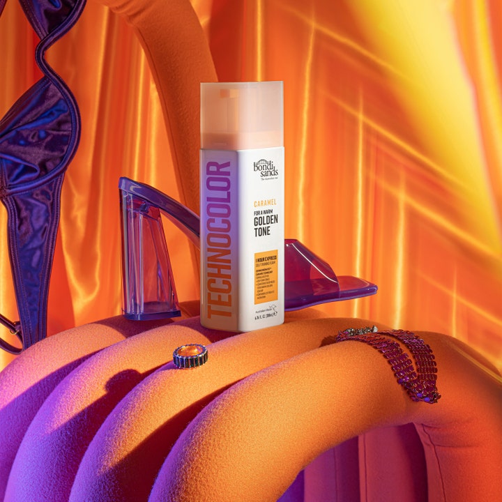 Bondi Sands Technocolor Face Serum Caramel 50 ml luo kultaisen sävyn violetin kengän ja korun rinnalla.