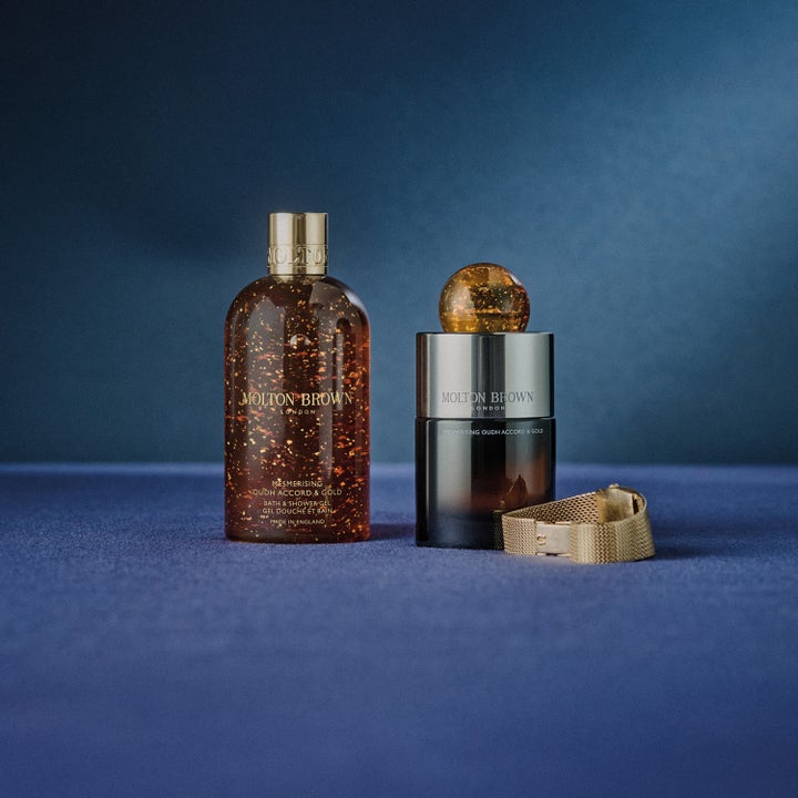 Molton Brown Mesmerising Oudh Accord & Gold 300 ml suihkugeeli ja hajuvesi sinisellä taustalla kultaisella kellolla
