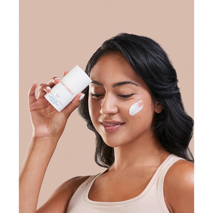 Exuviance Overnight Transformation Complex 50 g uudistava yövoide, nainen pitelee tuotetta ja voidetta poskella.