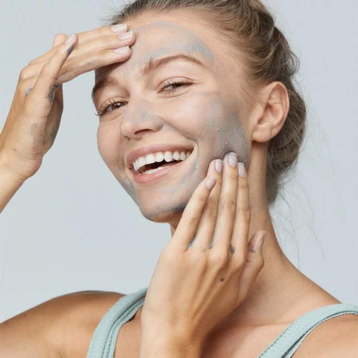 Dermalogica Daily Superfoliant 13 g kirkastava kasvokuorinta nainen levittää harmaata tahnaa kasvoilleen hymyillen