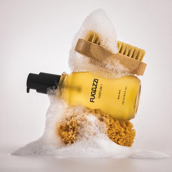 Fugazzi Parfum 1 Body Wash 250 ml suihkugeeli puhdistaa ihon valkoisen vaahdon, pesusienen ja puisen harjan keskellä.