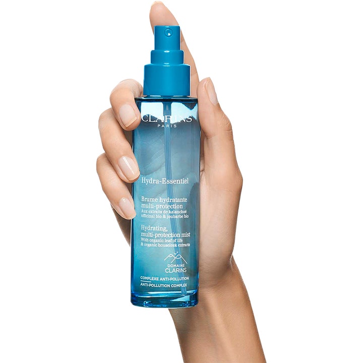 Clarins Hydra-Essentiel Hydrating multi-protection mist 75 ml kosteuttava kasvosuihke sinisessä pullossa kädessä
