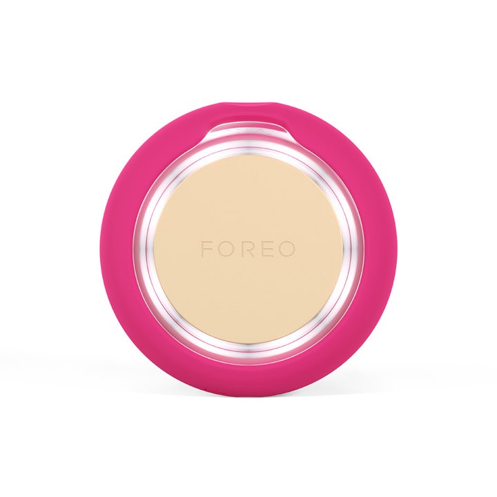 FOREO UFO™ 3 mini Fuchsia 1 kpl syväkosteuttava kasvohoitolaite on pyöreä fuksianpunainen laite kultaisella pinnalla.